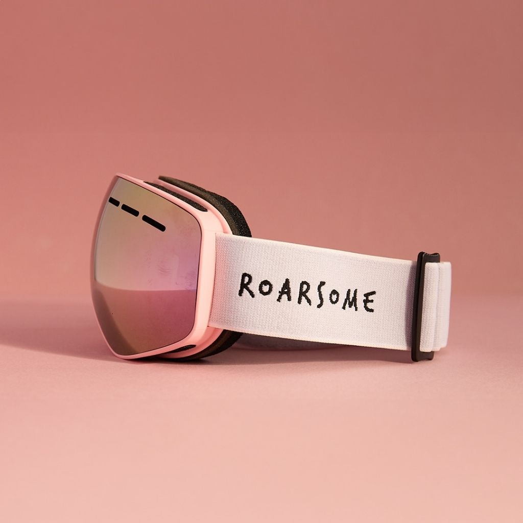 Pink ski goggles with 'ROARSOME' strap on a pink background