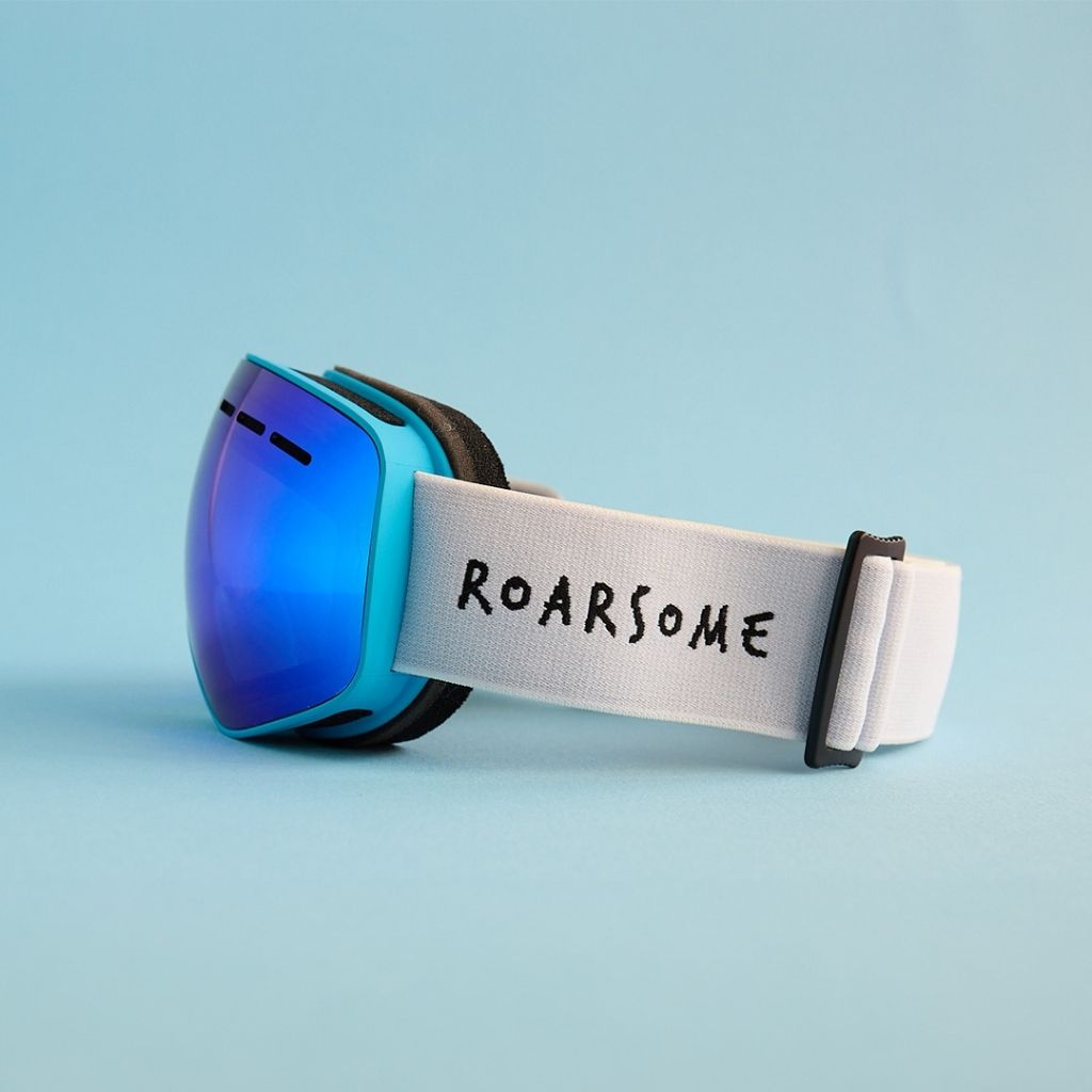 Blue ski goggles with 'ROARSOME' strap on a light blue background