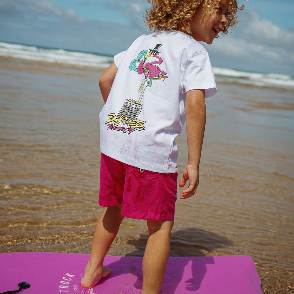 Little boy from the back on a surfboard wearing the Boardies Paradise City Kids T-Shirt
