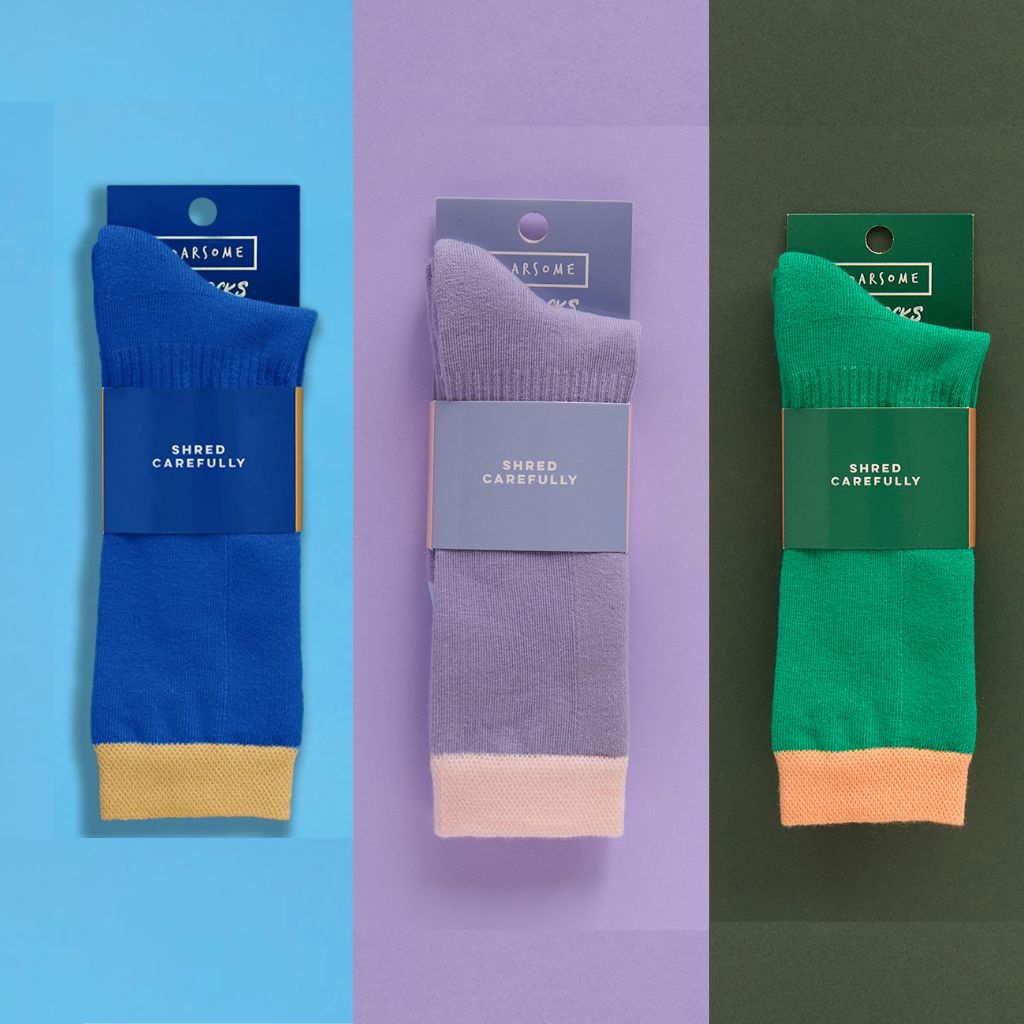 Three pairs of socks in blue, purple, and green with matching packaging on a multicolored background from Roarsome