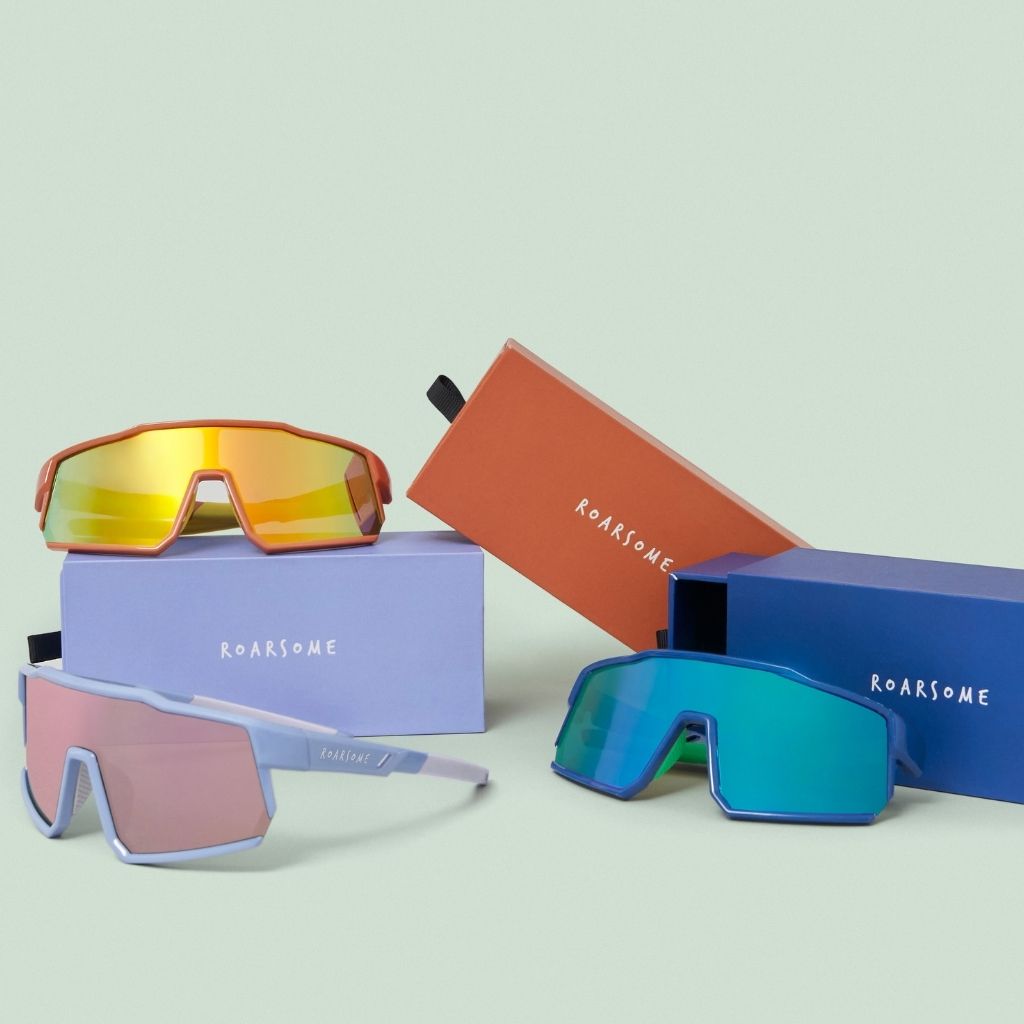 Colorful sunglasses with their packaging on a light green background from Roarsome
